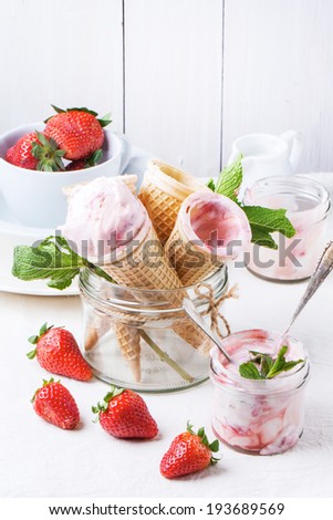 Wafer cones with strawberry ice cream with mint and fresh strawberries served in glass jar over white textile. See series