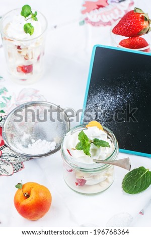 Dessert Eton mess with merengue, berries and whipped cream, served in glass jar on table with empty chalkboard.
