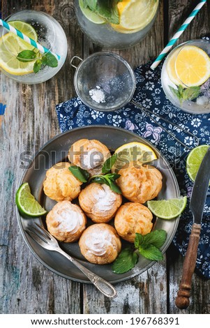 Vintage plate of homemade cakes profiteroles served with lemonade on old wooden table