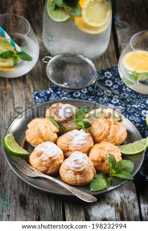 Vintage plate of homemade cakes profiteroles served with lemonade on old wooden table