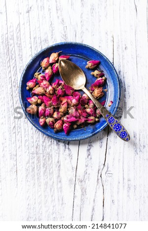 Blue ceramic plate of tea roses and golden tea spoon over white wooden background.. Top view. See series