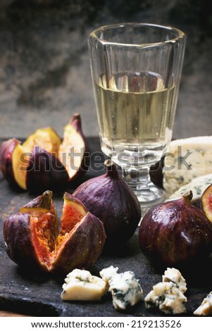 Figs with blue cheese, white wine and crackers on black cutting board. See series.
