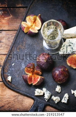 Figs with blue cheese, white wine and crackers on black cutting board. Top view. See series.