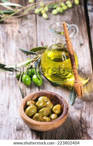 Green olives in olive wood bowl and bottle of olive oil served on old wooden table