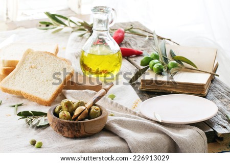 Lunch with green olives, bread and olive oil served with vintage book on old wooden table near window.