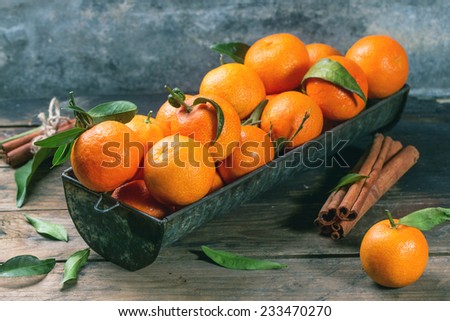 Tangerines with leaves and cinnamon stick on old wooden table.