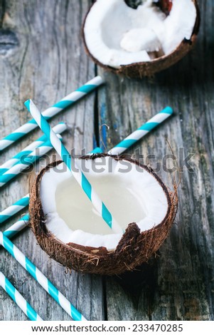 Broken coconut with coconut milk and vintage cocktail tubes on old wooden table