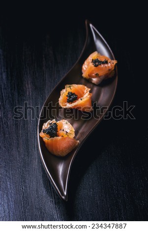 Plate of salmon rolls with black caviar over black textured surface