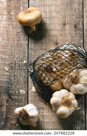 Mesh bag of smoked garlic over wooden background. Top view. See series