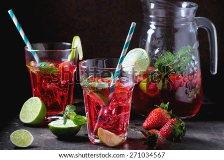 Two glasses with retro coctail tubes and glass jug of strawberry lemonade, served with fresh strawberries, mint and  lime over dark background. See series