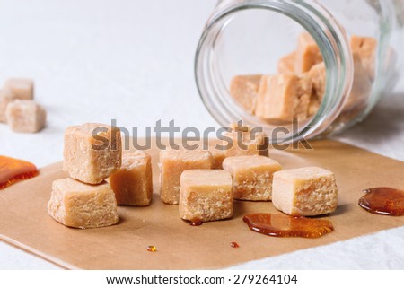 Fudge candy and caramel on baking paper and in glass jar, served over white tablecloth with jar of brown sugar