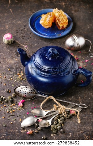 Blue ceramic teapot and plate with honeycombs, served with spoons, black and green tea lives over dark background