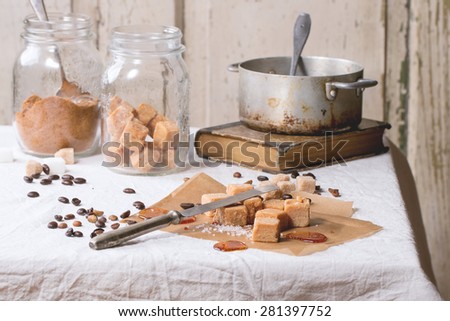 Fudge candy, coffee beans and caramel on baking paper, served over white tablecloth with vintage knife, jar of brown sugar and old pan