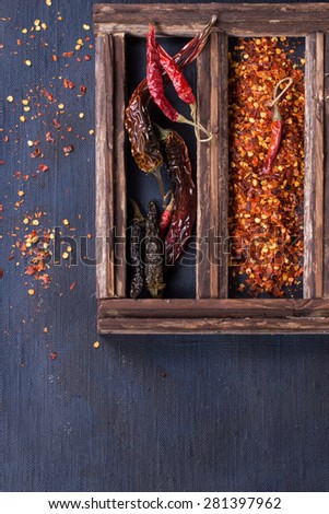 Assortment of dryed whole and flakes red hot chili peppers in wooden box over dark blue canvas as background