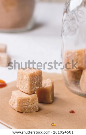 Close up of fudge candy and caramel on baking paper and in glass jar, served over white tablecloth
