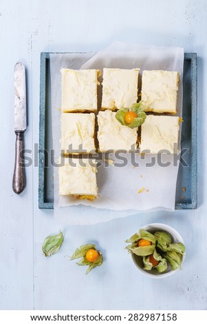 Homemade sliced cake with creamy mousse and tropical fruits mango and physalis served in wooden tray over light blue background. Top view