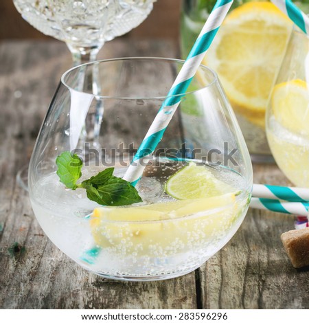 Fresh homemade lemonade with lemon, lime and mint in glasses with vintage cocktail tube over wooden table. Selective focus, square image