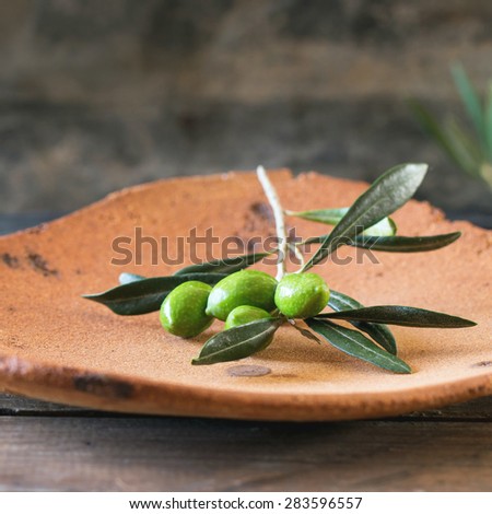 Green and black olive branch on clay plateover wooden table. Selective focus, square image