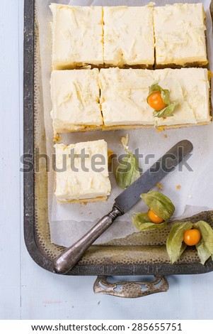 Homemade sliced cake with creamy mousse and tropical fruits mango and physalis served in vintage metal tray over light blue background. Top view