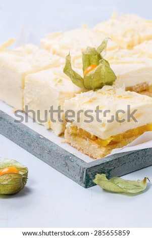 Homemade sliced cake with creamy mousse and tropical fruits mango and physalis served in wooden tray over light blue background