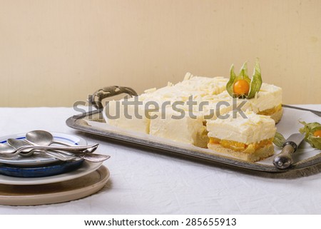 Homemade sliced cake with creamy mousse and tropical fruits mango and physalis served in vintage metal tray over white table. Selective focus