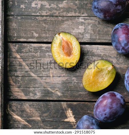 Whole and sliced plums over old wooden table. Top view. Square image