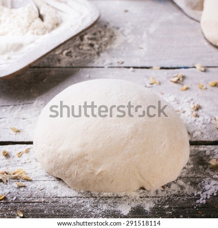 Baking bread. Dough on wooden table with flour, rolling-pin and jars with backing ingredients. Square image with selective focus