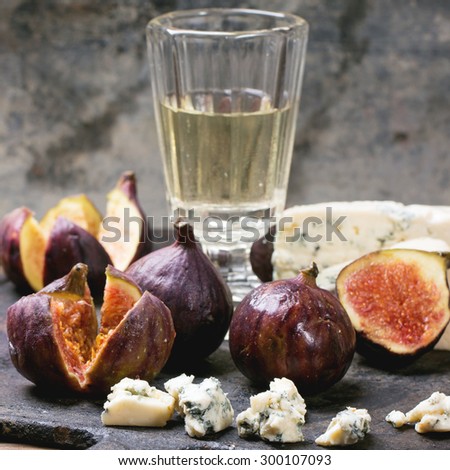 Figs with blue cheese, white wine and crackers on black cutting board. Square image with selective focus