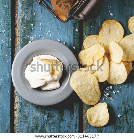 Top view on potato chips with plate of sause and sea salt over blue wooden table. Square image