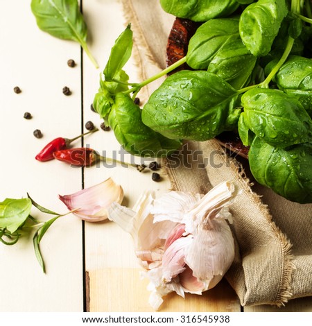 Bunch of fresh basil, bowl of walnuts, pepper and garlic served on white wooden table. Square image with selective focus
