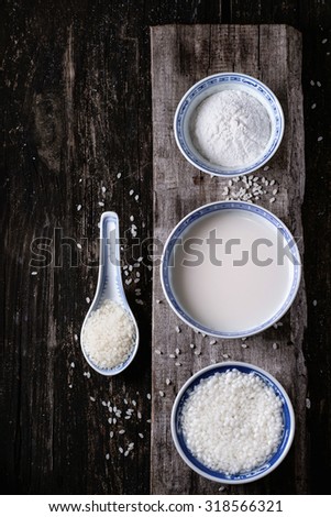 China style bowls with rice milk, rice flour and soaked rice over old wooden background with rice grains above. Top view.