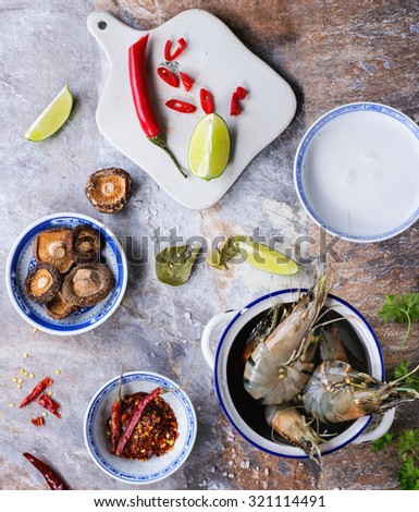 Ingredients for spicy Thai soup Tom Yam coconut milk, chili peppers, shiitake mushrooms and shrimps in ceramic bowls over stone background. Top view.
