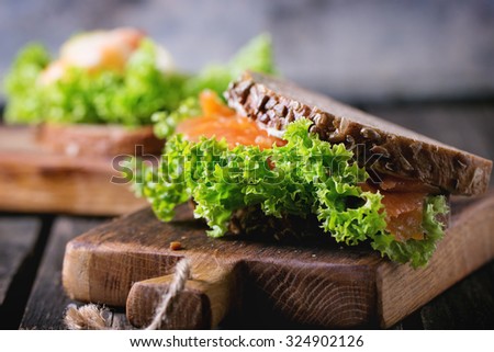 Sandwiches with whole wheat bread, fresh salad, shrimp and salted salmon on little wooden cutting board over old wooden table. Rustic style. Selective focus on salad