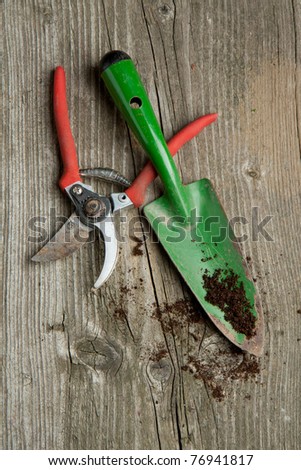 Green garden spade and scissors with ground on old wooden desk
