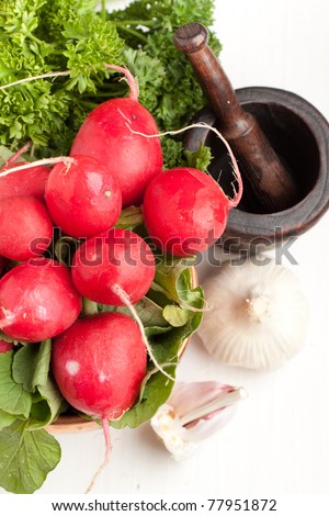 Top view on bunch of fresh radishes with garlic, parsley and vintage mortar on white table