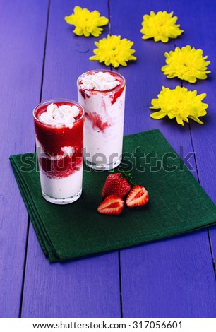 Delicious strawberry ice cream stands on a blue wooden table. Yellow flowers. Wooden board rustic