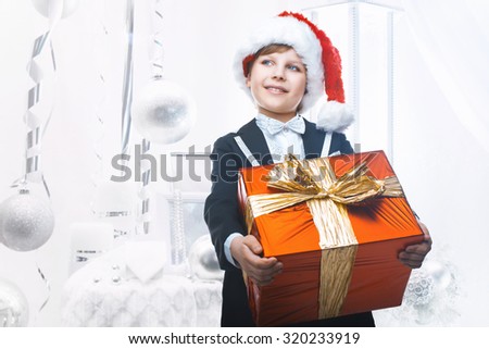 Beautiful little boy with a big Christmas gift in a Santa Claus hat. Christmas gifts for children. Smart boy Celebrates Christmas. New Year's holidays