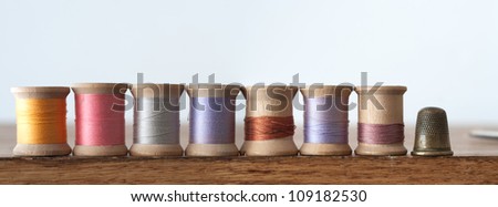 Row of various colored spools of thread with thimble in horizontal banner
