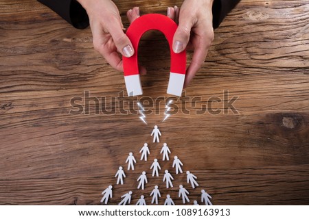 Businessperson's Hand Attracting Human Figures With Horseshoe Magnet On Wooden Desk Foto stock © 