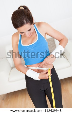 Happy woman measuring her waist with a tape measure to see if she has lost any weight after dieting and exercise
