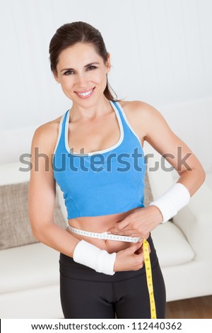 Happy woman measuring her waist with a tape measure to see if she has lost any weight after dieting and exercise