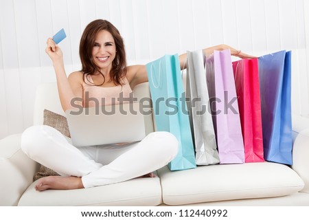 Young Woman Sitting On Sofa Shopping Online With Shopping Bags.