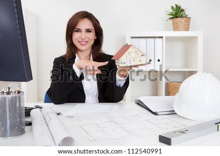 Portrait of a businessman pointing at home model with blueprints on office desk