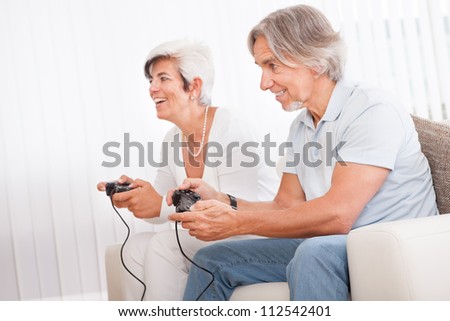 Excited middle-aged couple sitting on a sofa in their living room in front of the television screen playing computer games
