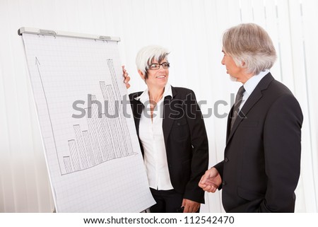 Businesswoman giving a presentation to her male colleague drawing a bar graph on a board as they analyze performance and discuss strategy