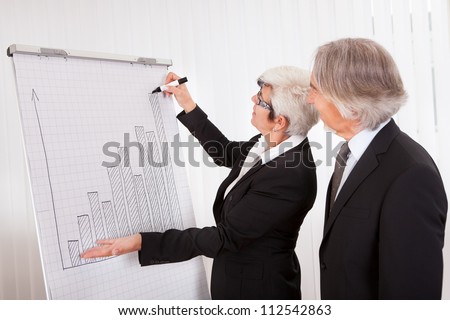 Businesswoman giving a presentation to her male colleague drawing a bar graph on a board as they analyze performance and discuss strategy