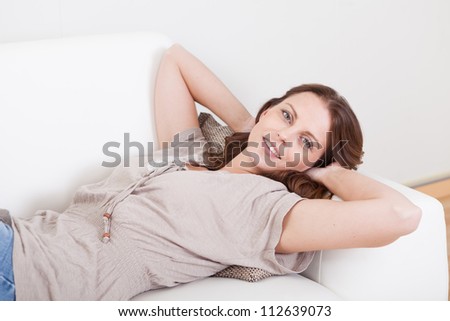 Casual barefoot woman in jeans lying on a couch in her living room with a cheerful smile