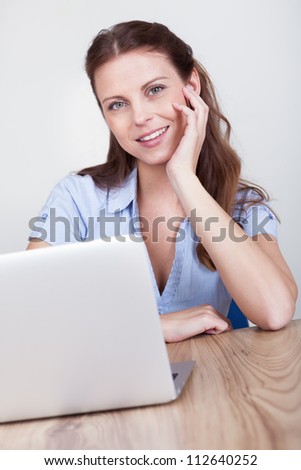 Friendly smiling woman sitting at a wooden table working at a laptop
