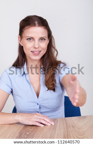 Young woman seated at a table offering to shake hands in welcome or in order to seal a business deal or transaction