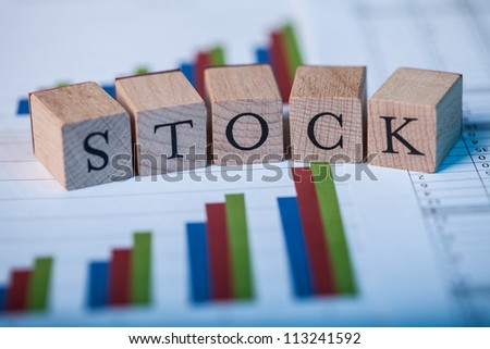 Wooden blocks with the lettering Stock on top of ascending bar graphs analyzing the statics and performance of shares within the market